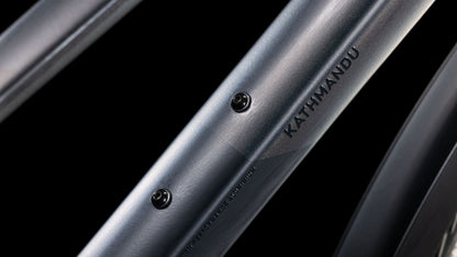 Nahaufnahme des Rahmenrohrs des Cube Kathmandu SLX nightsky'n'ink Trapeze 2025 von CUBE mit dem Schriftzug "KATHMANDU" und zwei Befestigungslöchern auf schwarzem Hintergrund - für umweltfreundliche Mobilität.