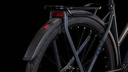 Die Nahaufnahme des Hinterrads des CUBE Cube Kathmandu SLX nightsky'n'ink Trapeze 2025 zeigt eine Shimano Cues 2x11-Gang Schaltung, schwarze Schutzbleche, einen Gepäckträger und zwei rote Reflektoren. Rahmen- und Reifendetails heben sich von einem schwarzen Hintergrund ab.