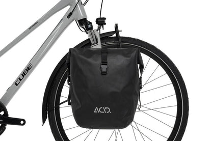 Eine Nahaufnahme des Hinterrads eines Fahrrads mit dem schwarzen ACID Gepäckträger LOWRIDER Suspension MTB und einer passenden wasserdichten Gepäckträgertasche, beides von ACID, auf einem hellgrauen CUBE Rahmen, wie man ihn in einem CUBE Store in Göttingen oder Hildesheim erwarten würde.