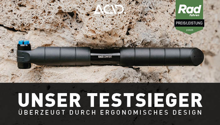 Eine schwarze ACID Pumpe RACE COMFORT von ACID ist auf einem groben Stein montiert. Oben befindet sich das ACID-Logo, rechts daneben zeigt eine grüne Plakette Rad fahren PREIS/LEISTUNG 2/2023. Der große Text lautet: UNSER TESTSIEGER - mit 2-Wege Pumpsystem und ergonomischem Design.